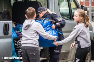 policjantka wspólnie z dziećmi pakują worki do busa